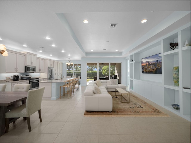 living area featuring visible vents, built in features, recessed lighting, a tray ceiling, and light tile patterned floors
