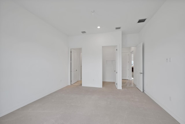 unfurnished bedroom featuring baseboards, visible vents, light carpet, and a walk in closet