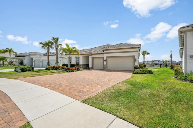 prairie-style home with a front yard, decorative driveway, an attached garage, stone siding, and stucco siding