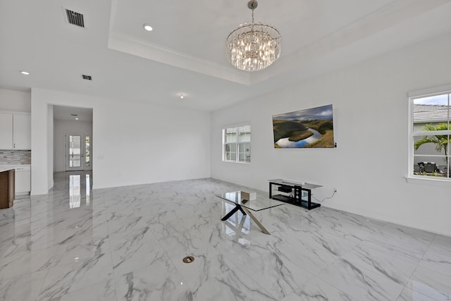 unfurnished living room featuring a chandelier, visible vents, a healthy amount of sunlight, and a raised ceiling