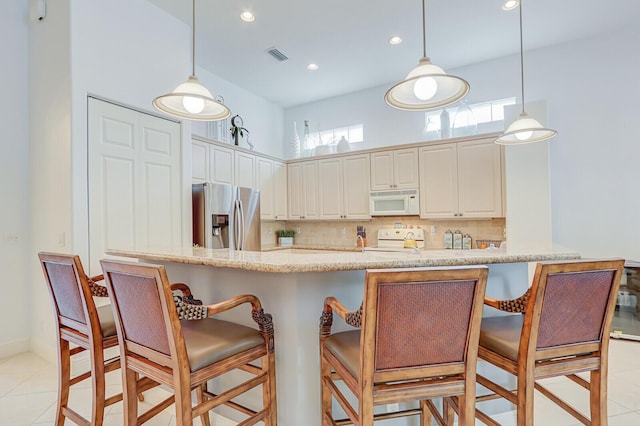 kitchen featuring stove, visible vents, white microwave, stainless steel fridge, and decorative backsplash