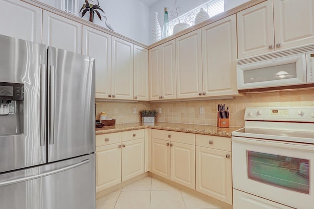 kitchen with light tile patterned floors, white appliances, light stone countertops, and tasteful backsplash
