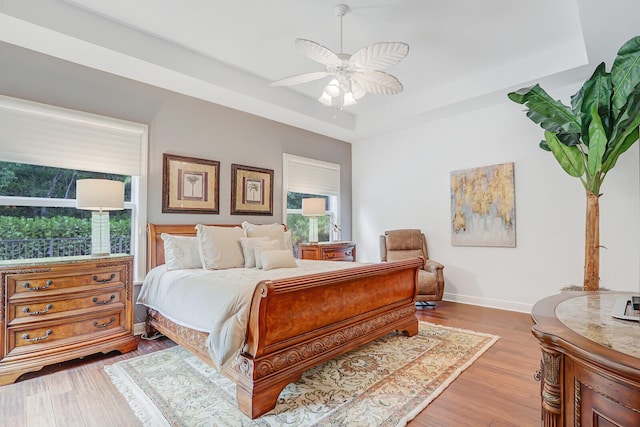 bedroom featuring baseboards, a tray ceiling, a ceiling fan, and wood finished floors