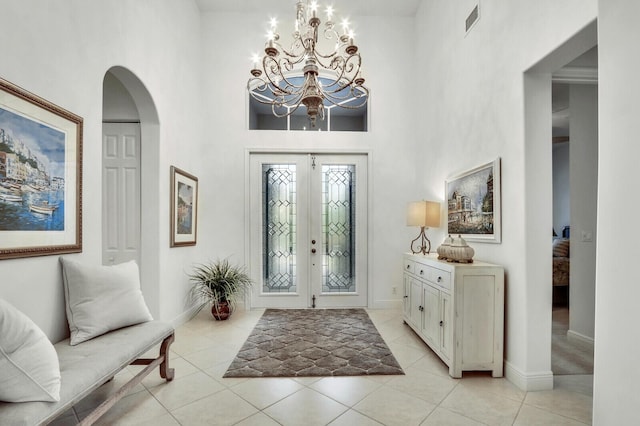 entryway featuring french doors, light tile patterned flooring, arched walkways, a high ceiling, and a notable chandelier