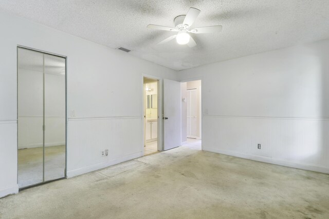 unfurnished bedroom featuring visible vents, a closet, a textured ceiling, a wainscoted wall, and carpet flooring