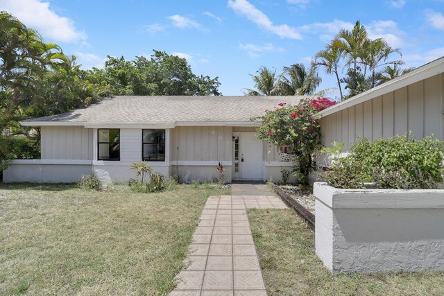 ranch-style house featuring a shingled roof and a front lawn