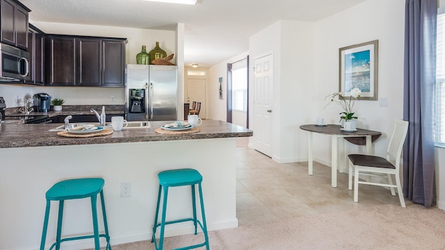 12134 SW Rimini Way, Port Saint Lucie, FL 34987 - kitchen featuring plenty of natural light, dark brown cabinetry, dark countertops, a breakfast bar, and stainless steel appliances