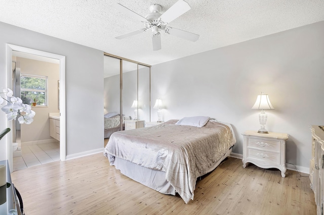 bedroom featuring baseboards, ensuite bath, light wood-style flooring, and a closet