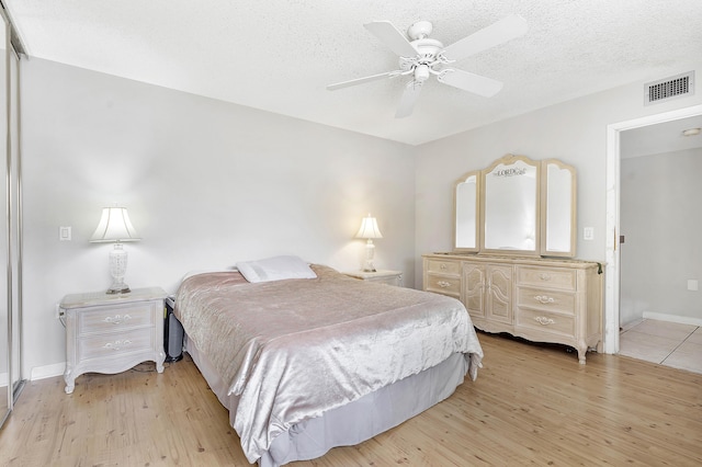 bedroom with a textured ceiling, baseboards, visible vents, and light wood-style floors