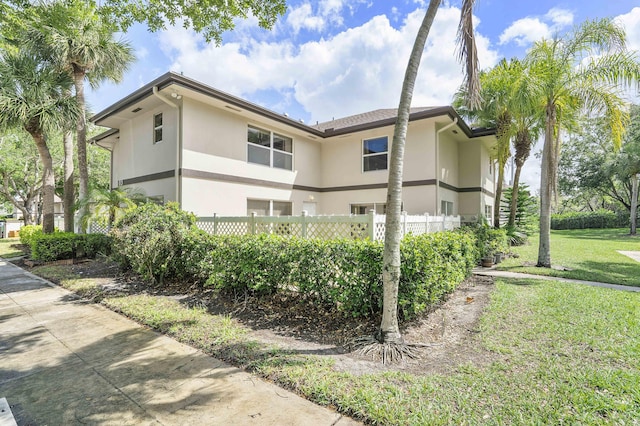 view of side of home featuring fence, stucco siding, and a yard