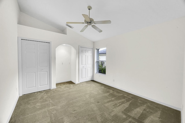 unfurnished bedroom featuring visible vents, multiple closets, arched walkways, carpet, and vaulted ceiling