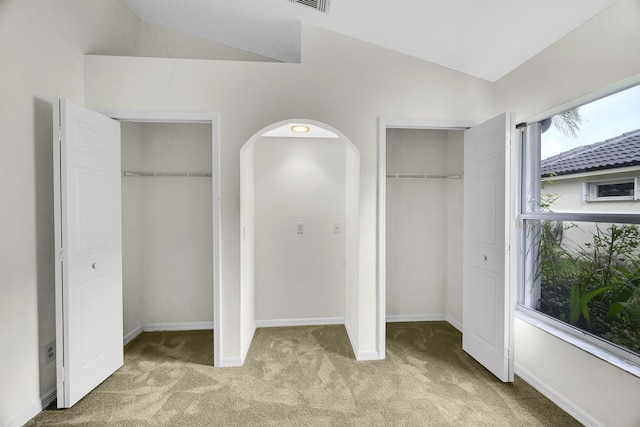 unfurnished bedroom with arched walkways, multiple closets, lofted ceiling, and light carpet