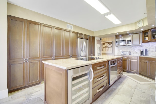 kitchen with light stone counters, black electric stovetop, stainless steel fridge with ice dispenser, beverage cooler, and a kitchen island