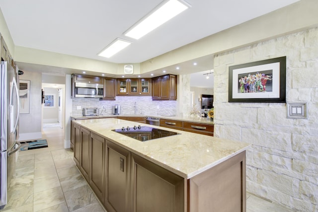 kitchen with light stone countertops, glass insert cabinets, a center island, appliances with stainless steel finishes, and backsplash
