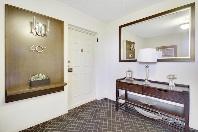 foyer entrance with baseboards, a textured ceiling, and dark colored carpet