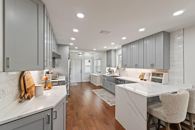 kitchen featuring light stone countertops, recessed lighting, tasteful backsplash, a sink, and gray cabinetry