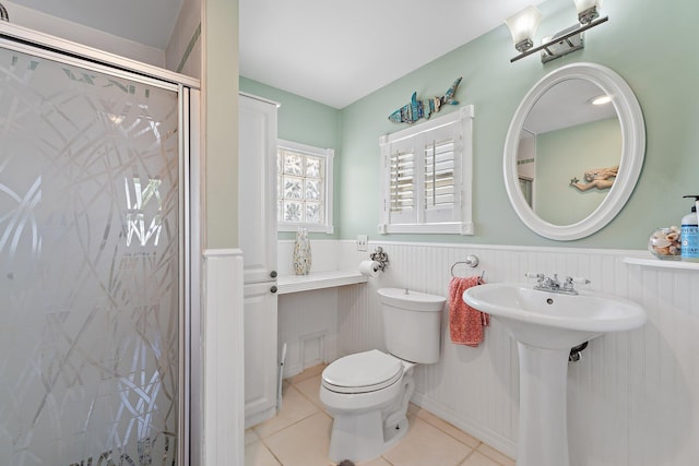 bathroom featuring wainscoting, toilet, tile patterned floors, a shower stall, and a sink