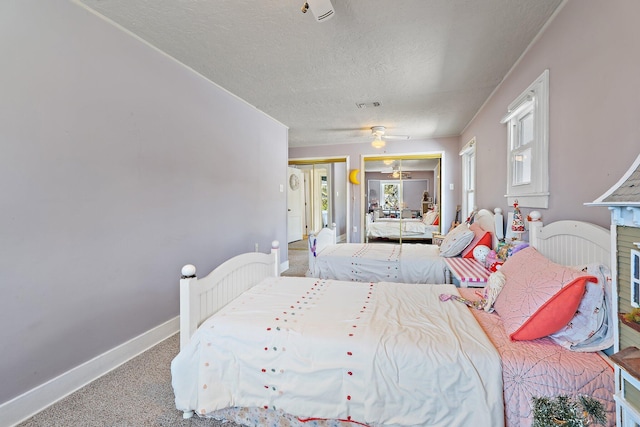 carpeted bedroom with baseboards, a ceiling fan, two closets, and a textured ceiling