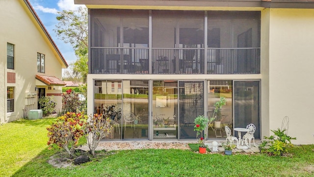 back of property with a lawn, central AC unit, stucco siding, and a sunroom