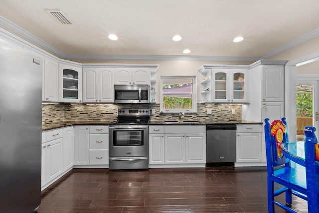 kitchen with stainless steel appliances, a sink, ornamental molding, glass insert cabinets, and open shelves
