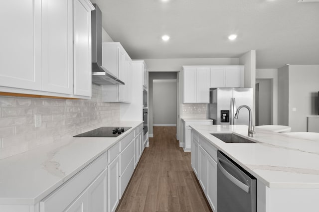 kitchen featuring wall chimney range hood, a sink, white cabinetry, a center island with sink, and black appliances