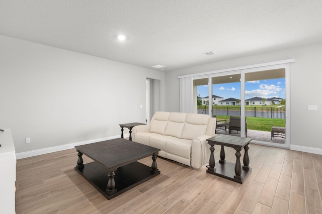 living area featuring a textured ceiling, baseboards, light wood-type flooring, a water view, and visible vents