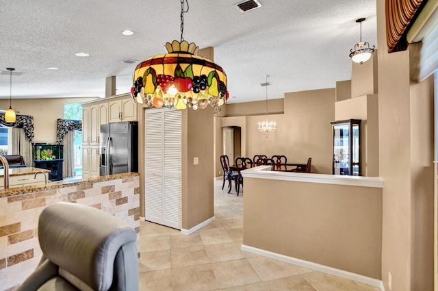 kitchen with cream cabinets, stainless steel fridge, a textured ceiling, visible vents, and pendant lighting