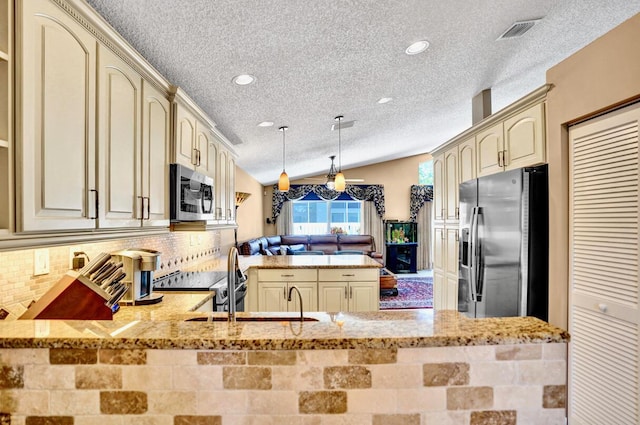 kitchen with a peninsula, a textured ceiling, cream cabinetry, appliances with stainless steel finishes, and vaulted ceiling