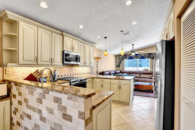 kitchen featuring a textured ceiling, cream cabinets, light stone counters, a peninsula, and stainless steel appliances