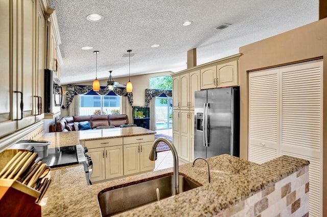 kitchen featuring cream cabinets, appliances with stainless steel finishes, a sink, a textured ceiling, and a peninsula