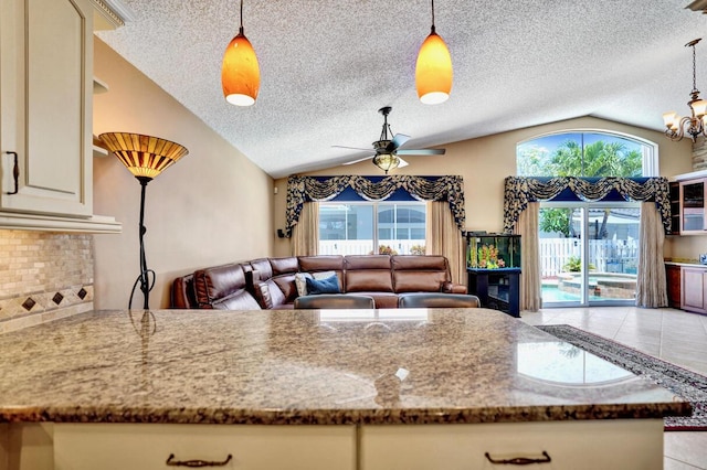 kitchen featuring a textured ceiling, vaulted ceiling, ceiling fan with notable chandelier, open floor plan, and stone counters