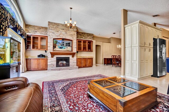 living room with an inviting chandelier, visible vents, light tile patterned flooring, a stone fireplace, and a textured ceiling