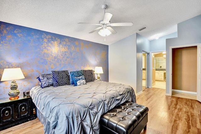 bedroom with a textured ceiling, visible vents, wood finished floors, baseboards, and wallpapered walls