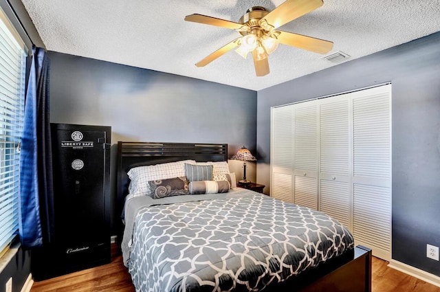 bedroom with a textured ceiling, baseboards, wood finished floors, visible vents, and a closet