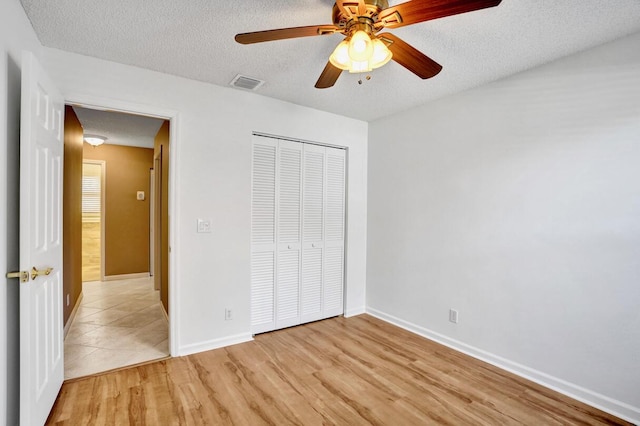 unfurnished bedroom with a closet, a textured ceiling, visible vents, and light wood-style floors