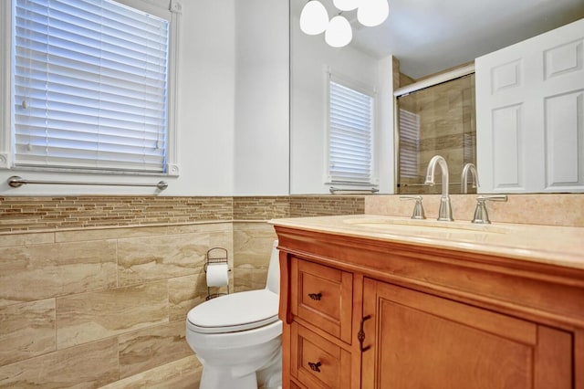 full bath featuring tile walls, wainscoting, a stall shower, vanity, and toilet