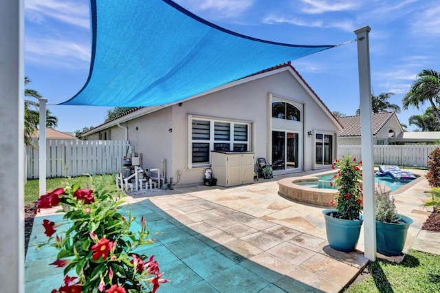 back of property featuring an in ground hot tub, fence, a patio area, and stucco siding