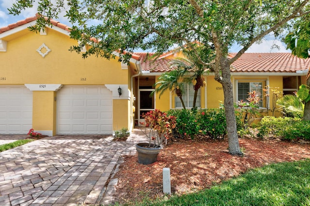 view of front of house featuring decorative driveway, a garage, a tile roof, and stucco siding