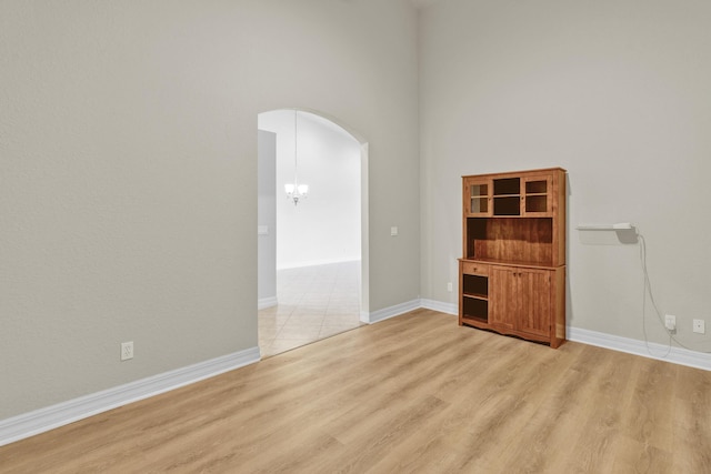unfurnished room with arched walkways, a high ceiling, baseboards, and light wood finished floors