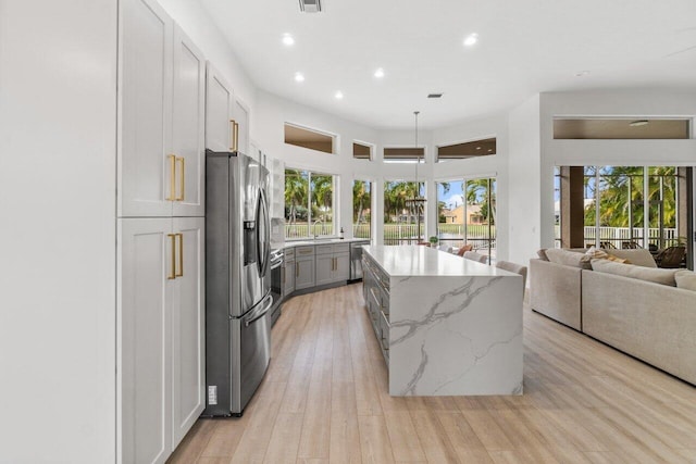 kitchen featuring a kitchen island, recessed lighting, light wood-type flooring, light stone counters, and stainless steel appliances