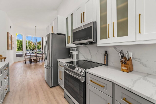 kitchen featuring light stone countertops, glass insert cabinets, light wood finished floors, backsplash, and stainless steel appliances