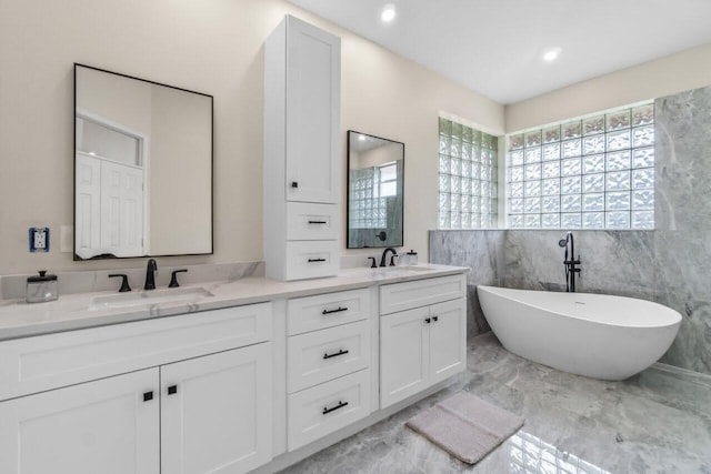 full bath with double vanity, a sink, marble finish floor, and a freestanding tub