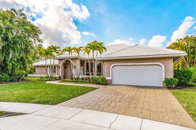 view of front of house with decorative driveway, an attached garage, a front yard, and stucco siding