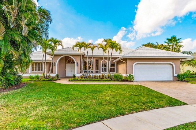 view of front facade with a front yard, stucco siding, an attached garage, driveway, and a tile roof
