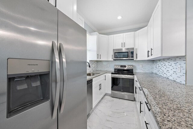 kitchen featuring white cabinets, light stone counters, a sink, marble finish floor, and stainless steel appliances