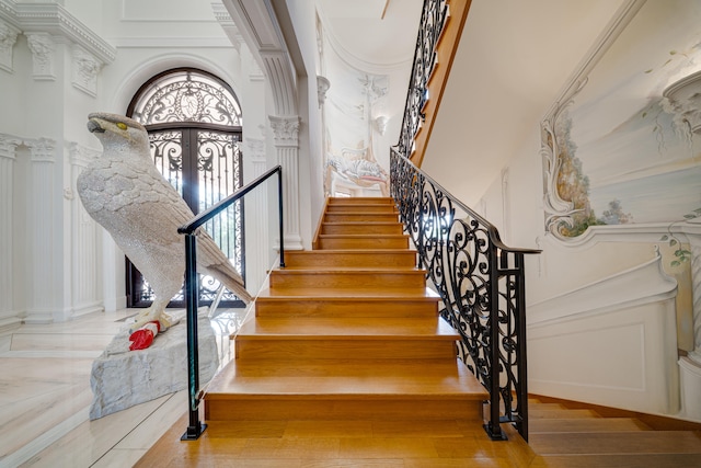 staircase with a high ceiling, decorative columns, and wood finished floors