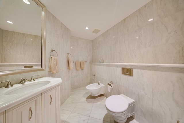 bathroom with visible vents, vanity, toilet, tile walls, and a bidet