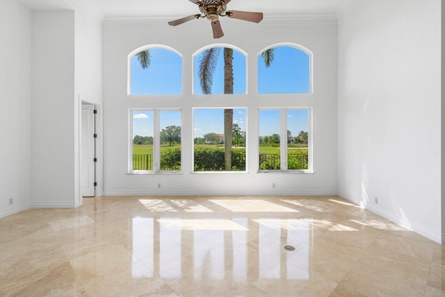 spare room featuring baseboards, ornamental molding, ceiling fan, and a high ceiling