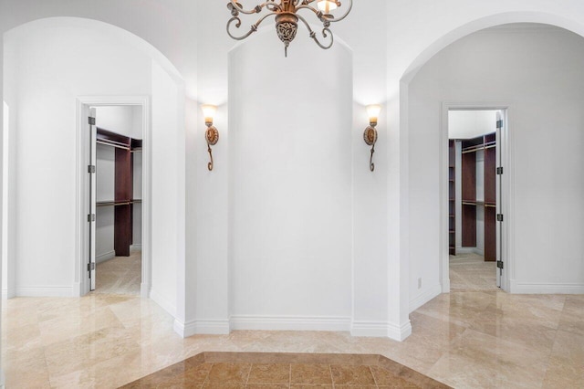 hallway with arched walkways, baseboards, a chandelier, and marble finish floor