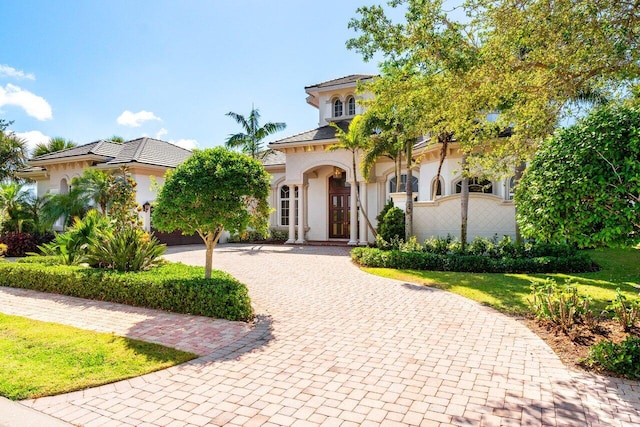 mediterranean / spanish-style house featuring curved driveway, a front lawn, and stucco siding